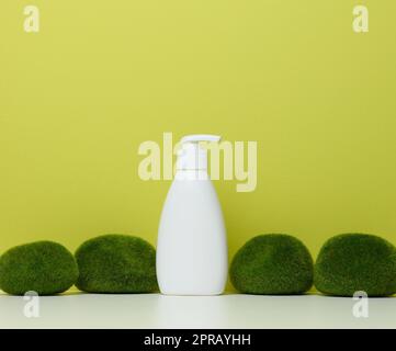 Weiße Kunststoffflasche mit Pumpe auf grünem Hintergrund. Behälter für Kosmetika Stockfoto