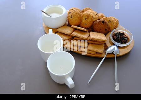 Ein leckerer Snack, zwei Tassen schwarzen Tee und ein Teller Haferbrei-Kekse, ein Holzbrett auf grauem Hintergrund, Blatttee. Stockfoto