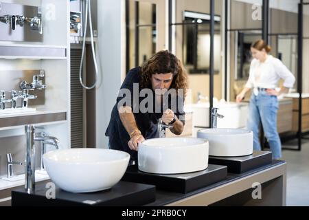 Ein Mann inspiziert und wählt einen neuen Küchen- oder Badezapfhahn im Baumarkt aus Stockfoto