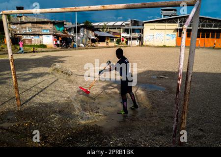 Ein junger afro-kolumbianischer Torhüter entfernt eine Pfütze Wasser, bevor er ein Fußballspiel auf einem Spielfeld in Quibdó, Chocó, Kolumbien, spielt. Stockfoto