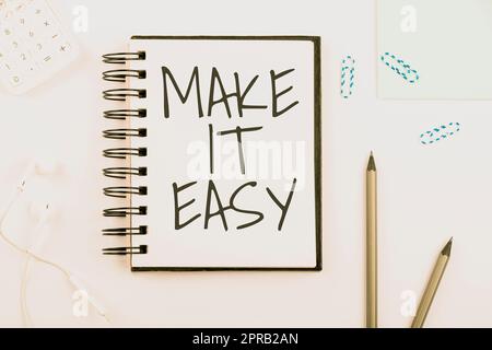 Textzeichen mit „Make IT Easy“. Geschäftsansatz intelligenter Ansatz mühelos ohne Sorgen oder Schwierigkeiten Notizbuch mit neuer Nachricht am Schreibtisch mit Stiften, Kopfhörern und Büroklammern. Stockfoto