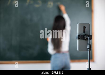 Asiatische Lehrer unterrichten an Bord, während sie online über Smartphone im Klassenzimmer Tafel-Vorlesungen halten Stockfoto