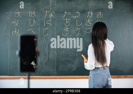 Asiatische Lehrer unterrichten an Bord, während sie online über Smartphone im Klassenzimmer Tafel-Vorlesungen halten Stockfoto