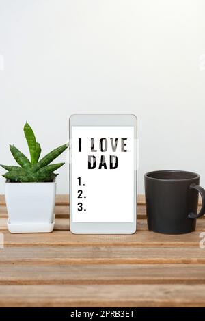 Textunterschrift mit „I Love Dad“. Ein Wort für gute Gefühle über die Zuneigung meines Vaters, die Glückseligkeit, die Tafel mit wichtigen Informationen auf dem Tisch mit Pflanzen und einer Tasse Kaffee. Stockfoto