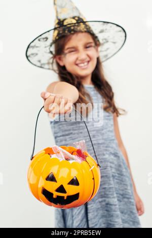 Ein kleines Mädchen, das einen Hexenhut trägt, während es einen Buben oder eine Laterne vor einem weißen Hintergrund hält. Stockfoto