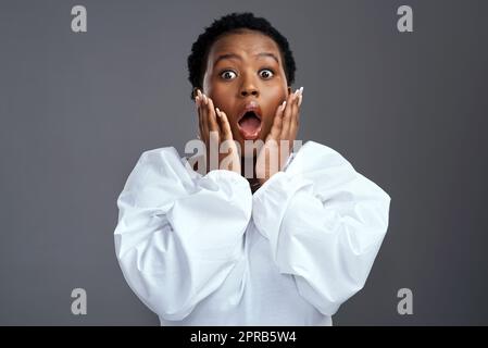 Haben Sie gehört? Eine Frau, die schockiert aussieht, während sie vor einem grauen Hintergrund steht. Stockfoto