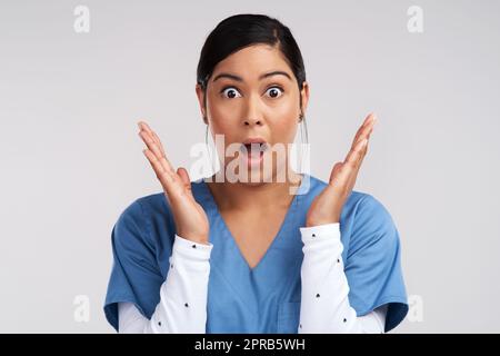 Tropfendes Pendel rollt sich.das zieht an eurer Welt. Porträt eines schockierten jungen Arztes in Scrubs vor weißem Hintergrund. Stockfoto