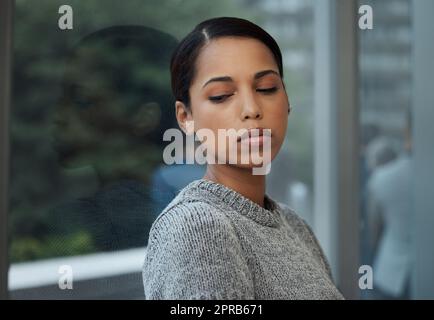 Träumen von weißen Stränden. Eine junge Geschäftsfrau, die eine Pause nimmt und sich an ein Fenster lehnt. Stockfoto