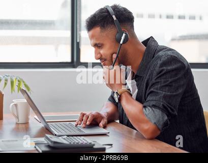Lassen Sie mich darüber nachdenken: Ein hübscher junger, männlicher Call Center-Agent, der bei der Arbeit an seinem Laptop nachdenklich aussieht. Stockfoto