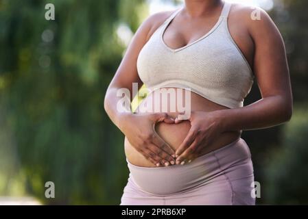 Meine Liebe zu Ihnen ist es, was mich motiviert, gesunde Entscheidungen zu treffen. Eine Frau, die eine Herzform auf ihrem schwanger Bauch bildet. Stockfoto