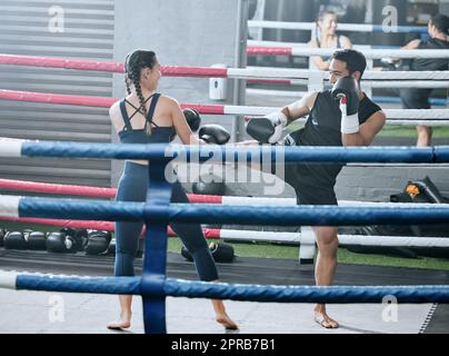 Fit, gesund und aktiv Frau macht Kickboxing Workout im Gym Sparring mit ihrem Personal Trainer in einem Wellnesscenter lernen zu kämpfen. Sportlicher Mann gegen Frau in einem Boxsport-Spiel in einem Ring Stockfoto