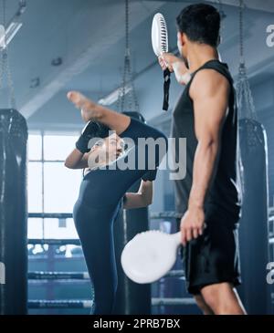 Kickboxen, Kampf und Kämpferin trainieren High-Kicks mit ihrem Trainer im Fitnessstudio. Eine Sportlerin, die Kampfkunst und Training führt, trainiert oder ein Workout für einen Kampf mit ihrem Trainer absolviert Stockfoto