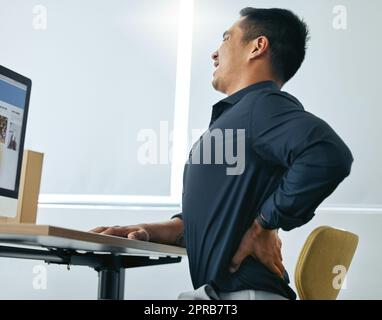 Autsch wie lange habe ich schon gesessen. Ein hübscher junger Geschäftsmann, der allein in seinem Büro sitzt und Rückenschmerzen hat. Stockfoto