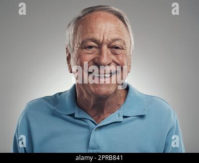 Es fühlt sich gut an, wieder zu lächeln. Ein Mann lächelt fröhlich vor grauem Hintergrund in einem Studio auf die Kamera. Stockfoto