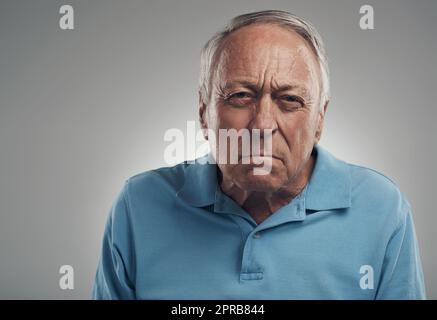 Du machst mich so wütend. Ein alter Mann schaut wütend auf die Kamera in einem Studio vor grauem Hintergrund. Stockfoto