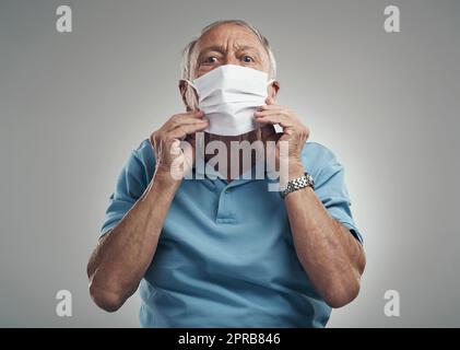 Bedecken Sie sowohl Ihren Mund als auch Ihre Nein. Ein älterer Mann trägt eine schützende Gesichtsmaske in einem Studio vor einem grauen Hintergrund. Stockfoto