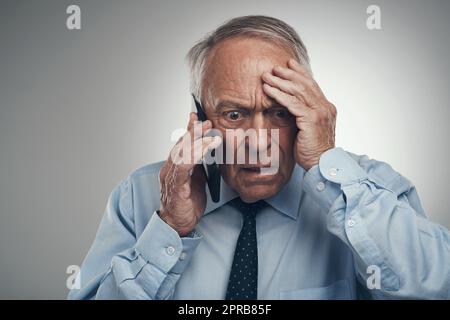 Das ist kein guter Anruf. Ein älterer Geschäftsmann, der allein vor einem grauen Studiohintergrund steht und gestresst aussieht, während er sein Handy benutzt. Stockfoto