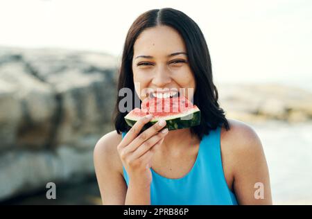 Frische, saftige Wassermelone ist eine der besten Früchte. Eine junge Frau, die am Strand ein Stück Wassermelone isst. Stockfoto