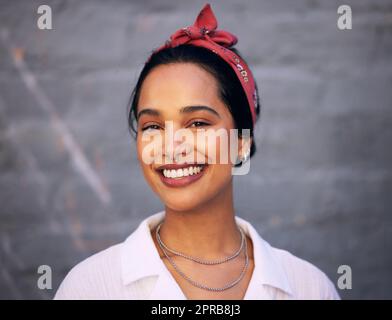 Glück lässt Sie wirklich glühen. Eine attraktive junge Frau, die tagsüber alleine draußen gegen eine graue Wand steht. Stockfoto