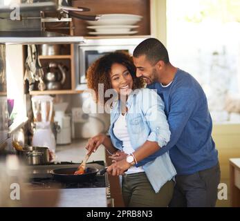 Das Abendessen hat fast meine Liebe getan. Aufnahme eines jungen Mannes, der seine Frau umarmt, während sie zu Hause eine Mahlzeit zubereitet. Stockfoto