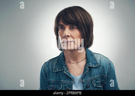 Sich in Gedanken verirrt. Studioaufnahme einer älteren Frau, die vor grauem Hintergrund nachdenklich aussieht. Stockfoto