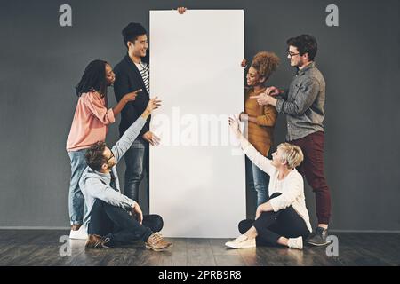 Eine vielfältige Gruppe von Personen, die ein leeres Whiteboard oder Poster halten und Werbetexte zeigen. Ein Team oder Freunde, die ein Plakat-Banner vermarkten, stehen und sitzen für eine Beförderung zusammen Stockfoto