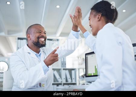 Die Wissenschaft rettet den Tag. Zwei Wissenschaftler geben sich gegenseitig eine hohe fünf, während sie in einem Labor forschen. Stockfoto