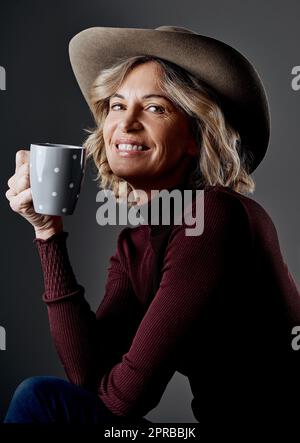 Das Leben wird besser mit einer Tasse grünem Tee. Eine reife Frau, die stilvoll vor einem grauen Hintergrund aussieht. Stockfoto