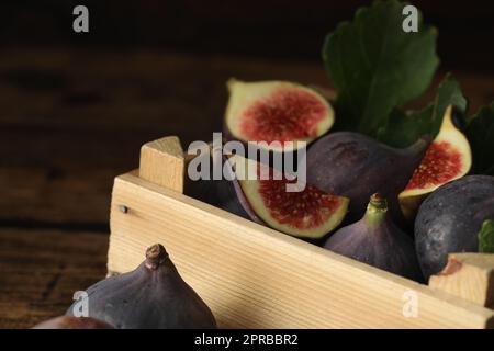 Ganze und geschnittene, leckere, frische Feigen in Holzkiste, Nahaufnahme Stockfoto