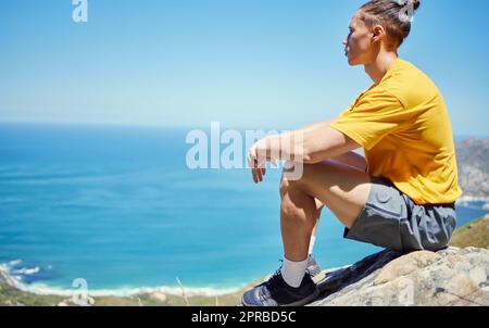Die Sonne fühlt sich so gut auf meiner Haut an. Ein junger Mann sitzt, um die Aussicht während einer Wanderung zu genießen. Stockfoto