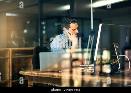 HES hat keine Angst vor harter Arbeit. Aufnahme eines jungen Geschäftsmannes, der während einer späten Nacht auf der Arbeit am Telefon sprach und einen Computer benutzte. Stockfoto