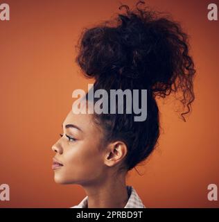 Je größer das Brötchen, desto größer die Träume. Eine junge Frau trägt ihre Haare in einem Brötchen vor einem orangen Hintergrund. Stockfoto