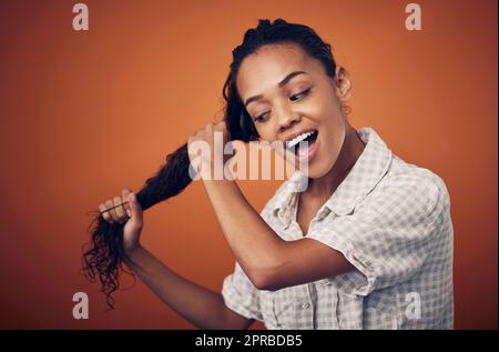 Ich bin dem Erreichen perfekter Locken einen Schritt näher. Eine junge Frau mit nassem Haar posiert vor einem orangen Hintergrund. Stockfoto