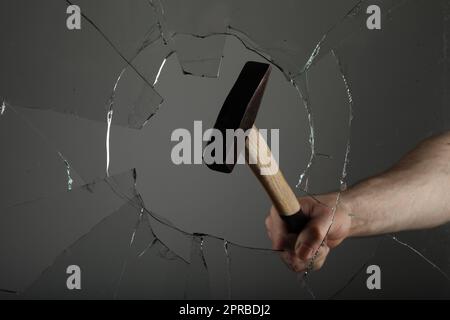 Ein Mann zertrümmert Fenster mit Hammer auf grauem Hintergrund, Nahaufnahme Stockfoto