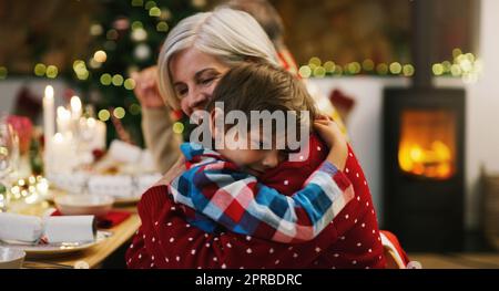 Mein Lieblingsweihnachtsgeschenk nennt mich Oma. Eine liebevolle ältere Frau umarmte ihren Enkel während einer Weihnachts-Dinner-Party zu Hause. Stockfoto