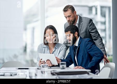 Eine Gruppe von Geschäftsleuten, die in einem Büro an einem digitalen Tablet arbeiten. Stockfoto