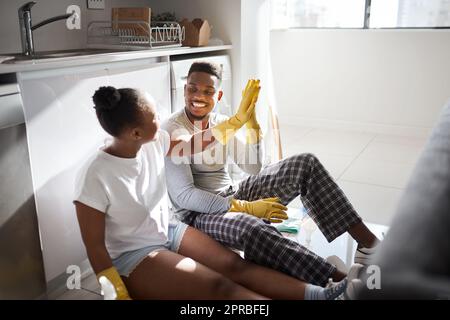 Teilen Sie die Aufgabe, teilen Sie die Belohnung. Ein junges Paar, das sich gegenseitig eine hohe fünf gibt, nachdem es zu Hause gemeinsam Aufgaben erledigt hat. Stockfoto