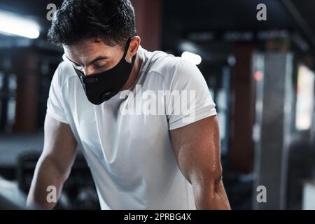 Ein hübscher und athletischer junger Mann, der beim Training im Fitnessstudio eine Maske trägt. Stockfoto