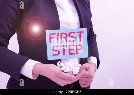 Inspiration mit Schild „erster Schritt“. Konzeptfoto zum Beginn eines bestimmten Prozesses oder einer Geschäftsfrau, die Papierverpackungen und wichtige Botschaft auf dem Stick in der Hand hält. Stockfoto