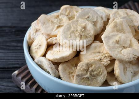 Schüssel mit getrockneten Bananenscheiben auf schwarzem Holztisch, Nahaufnahme Stockfoto