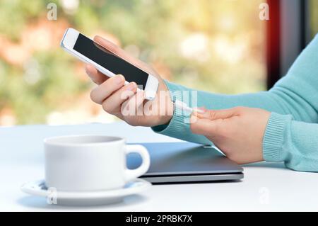 Mädchen Hand Smartphone in einer Tabelle zu Hause mit einem Fenster im Hintergrund Ladegerät anschließen Stockfoto
