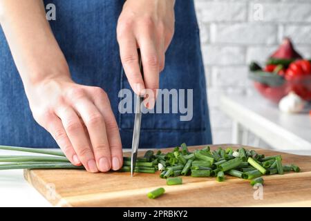 Frau schneidet grüne Frühlingszwiebeln auf Holzbrett, Nahaufnahme Stockfoto