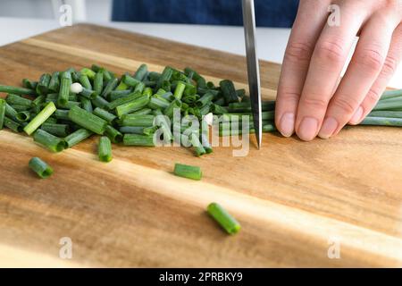 Frau schneidet grüne Frühlingszwiebeln auf Holzbrett, Nahaufnahme Stockfoto