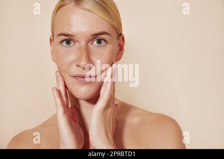 Weiblich mit Sommersprossen, die ihr Gesicht berühren. Porträt einer schönen blonden Frau, die in die Kamera schaut und ihr Gesicht massiert. Stockfoto