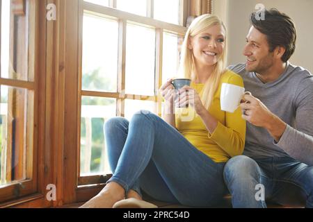 Du hast die Sahne in meinen Kaffee getan. Ein glückliches Paar, das ein heißes Getränk zusammen am Fenster zu Hause genießt. Stockfoto