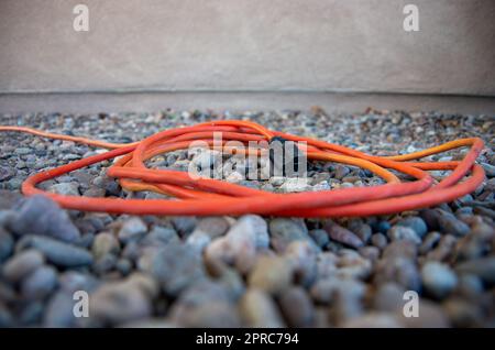 Orangefarbenes Verlängerungskabel für den Außenbereich im Felsenbett Stockfoto