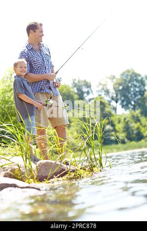 Nur zwei Jungs am See. Ein süßer Junge, der mit seinem Vater am See angeln und lächelt. Stockfoto