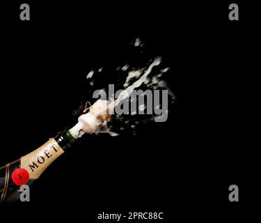 Nahaufnahme einer prallenden Moet-Champagnerflasche vor schwarzem Hintergrund. Stockfoto