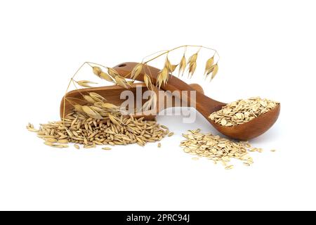 Haferkörner mit Rümpfen oder Schalen in Holzlöffel und Hafergrundeln gerollt und abgeflacht zu Flocken in Holzlöffel isoliert auf weißem Hintergrund Stockfoto