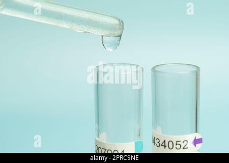 Nahaufnahme einer Pipette, die eine Probe auf blauem Hintergrund in ein Reagenzglas tropft. Stockfoto